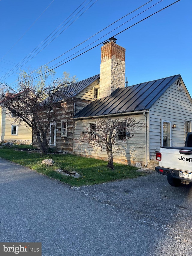 view of side of property with a chimney, a standing seam roof, and metal roof