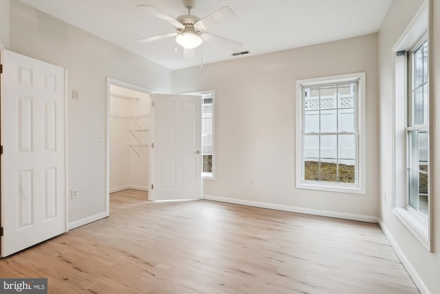 unfurnished bedroom with a ceiling fan, a walk in closet, light wood-style flooring, baseboards, and visible vents
