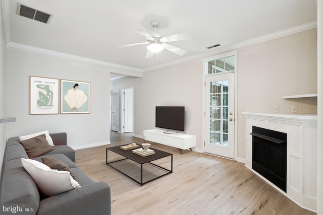 living room featuring baseboards, ornamental molding, light wood finished floors, and visible vents