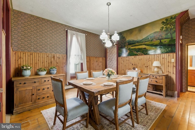 dining space with light wood-style flooring, wallpapered walls, and an inviting chandelier