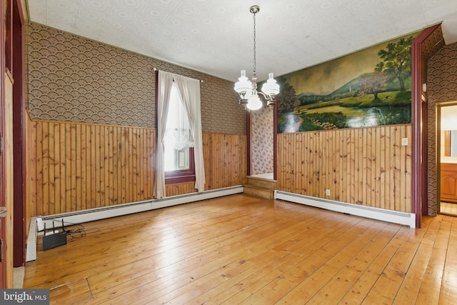 unfurnished dining area with a chandelier, hardwood / wood-style floors, a baseboard radiator, and wallpapered walls
