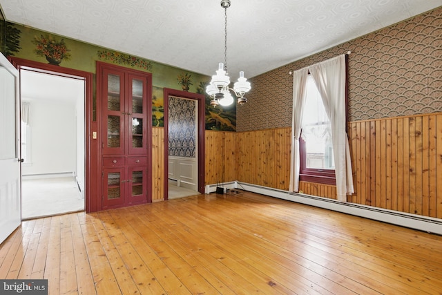 unfurnished dining area featuring light wood finished floors, wallpapered walls, an inviting chandelier, and wainscoting