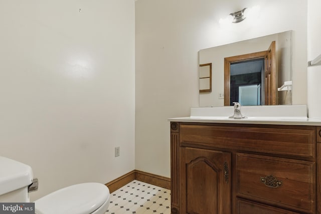half bath featuring tile patterned floors, vanity, baseboards, and toilet