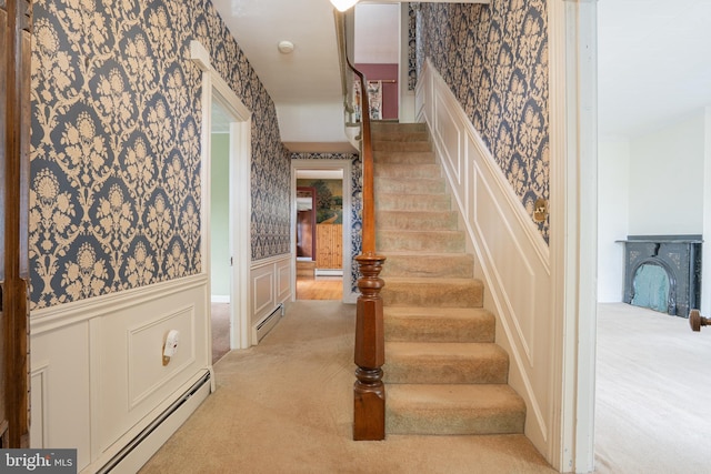 stairway with baseboard heating, wallpapered walls, a decorative wall, and a wainscoted wall