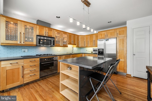 kitchen with open shelves, dark countertops, a breakfast bar area, appliances with stainless steel finishes, and light wood finished floors