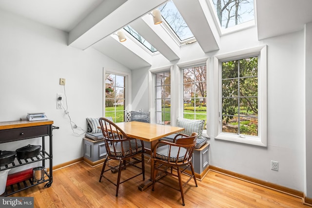 dining area with baseboards, light wood-type flooring, and lofted ceiling with skylight