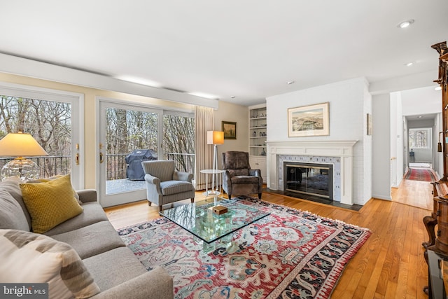 living room with hardwood / wood-style floors, a tile fireplace, built in shelves, and recessed lighting