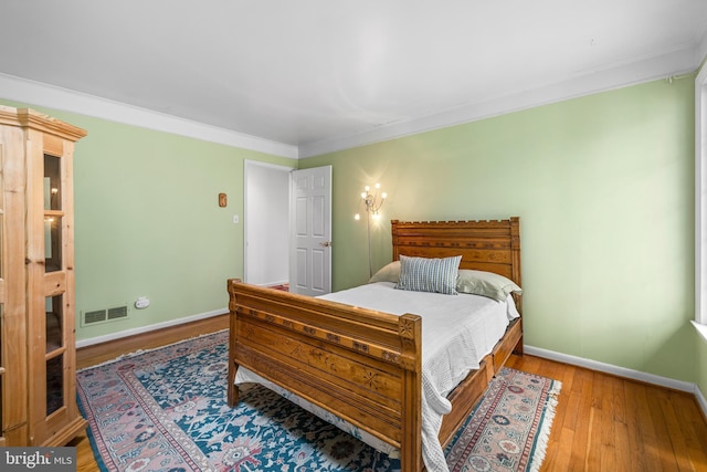 bedroom with crown molding, wood finished floors, baseboards, and visible vents
