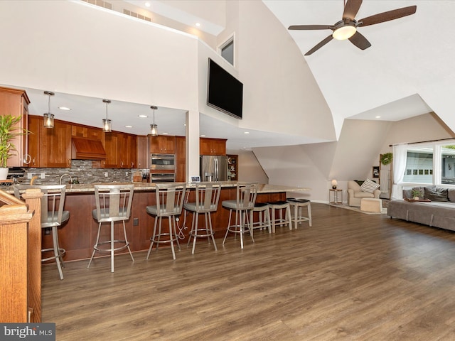 kitchen with open floor plan, custom exhaust hood, wood finished floors, a breakfast bar, and appliances with stainless steel finishes