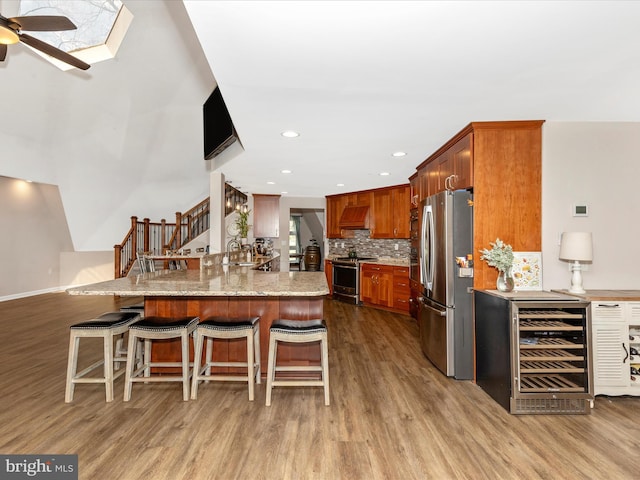 kitchen featuring ceiling fan, wood finished floors, beverage cooler, and appliances with stainless steel finishes