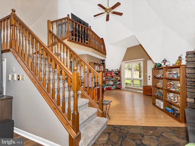 staircase with ceiling fan, a towering ceiling, wood finished floors, and baseboards