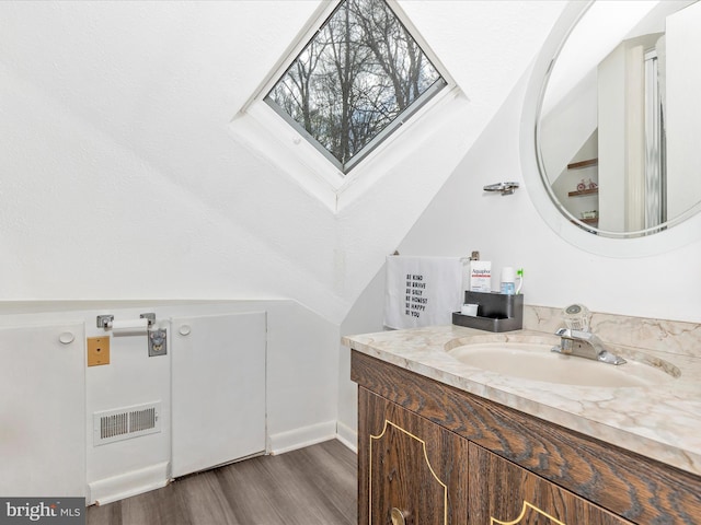 bathroom with lofted ceiling with skylight, wood finished floors, vanity, baseboards, and visible vents