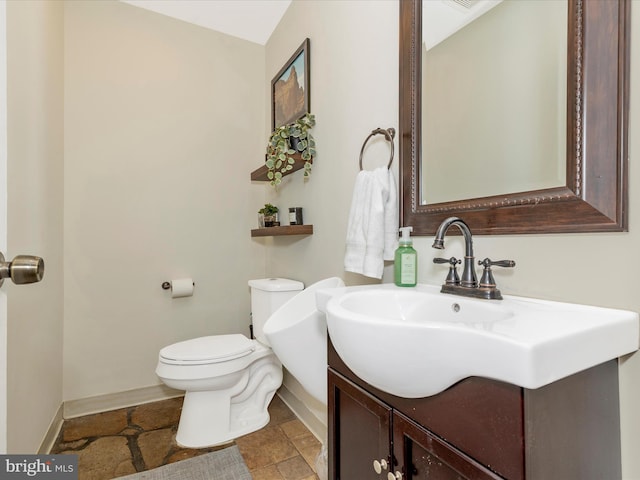 bathroom with baseboards, stone finish flooring, toilet, and vanity