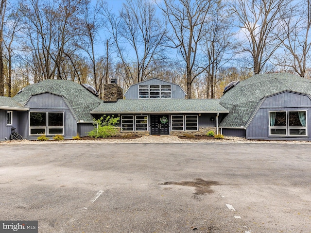 view of front of home with a chimney, a gambrel roof, and a shingled roof