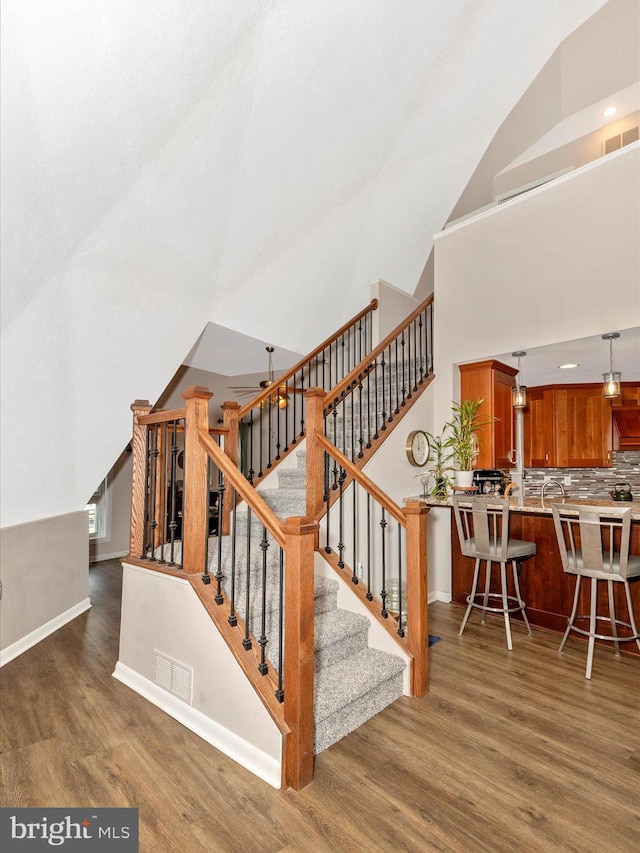 stairway featuring high vaulted ceiling, baseboards, wood finished floors, and visible vents