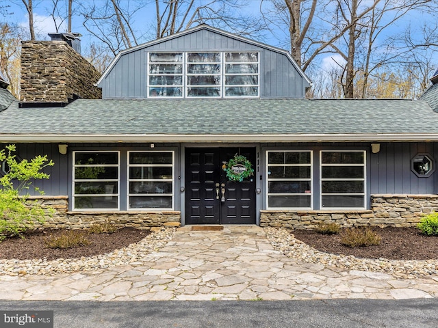 view of front of house featuring roof with shingles, stone siding, and a chimney