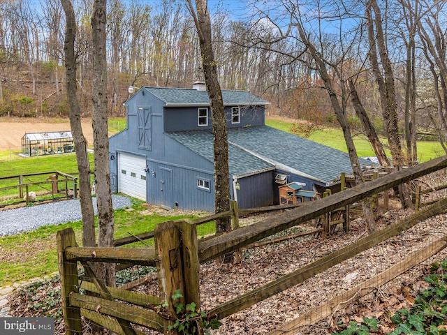 view of property exterior featuring a chimney, dirt driveway, an outdoor structure, fence, and roof with shingles