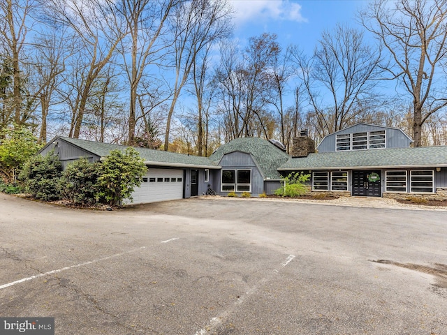 view of front of home featuring an attached garage, driveway, a shingled roof, and a chimney