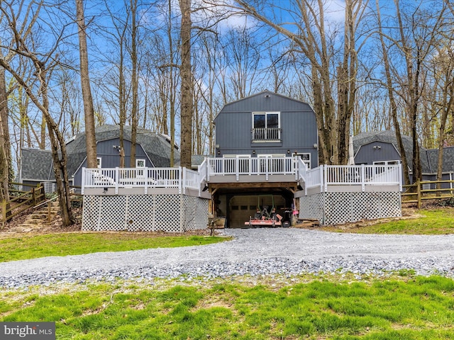 back of house with driveway, an attached garage, a gambrel roof, a deck, and an outdoor structure