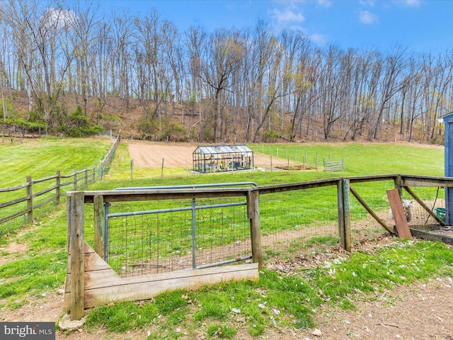 view of gate with a rural view, a greenhouse, and fence