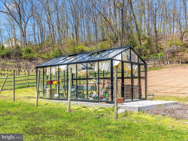 view of greenhouse with fence and a lawn