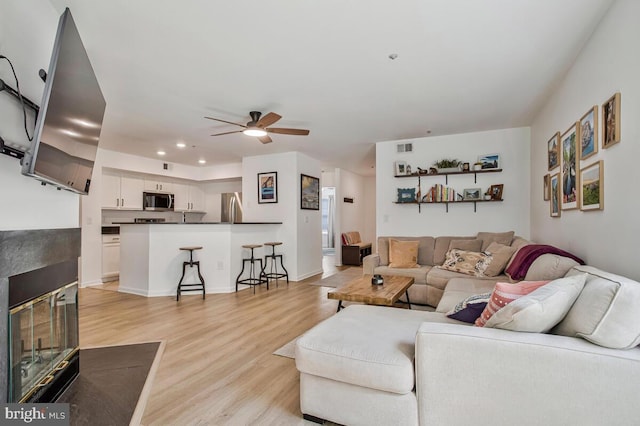 living room featuring light wood finished floors, a ceiling fan, recessed lighting, and a multi sided fireplace