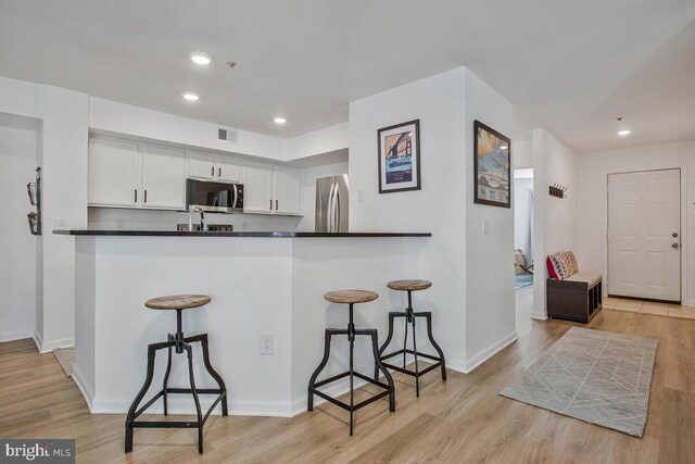 kitchen featuring appliances with stainless steel finishes, a kitchen bar, white cabinetry, light wood-style flooring, and recessed lighting