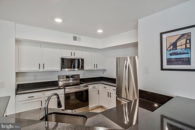 kitchen with stainless steel appliances, a sink, white cabinets, dark stone counters, and recessed lighting