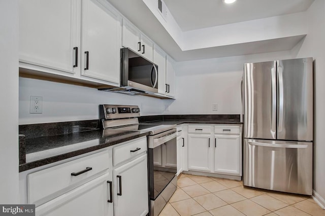 kitchen with appliances with stainless steel finishes, light tile patterned floors, white cabinetry, and dark stone counters
