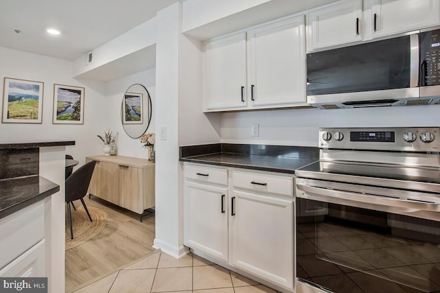 kitchen with appliances with stainless steel finishes, white cabinets, light tile patterned floors, dark stone counters, and recessed lighting