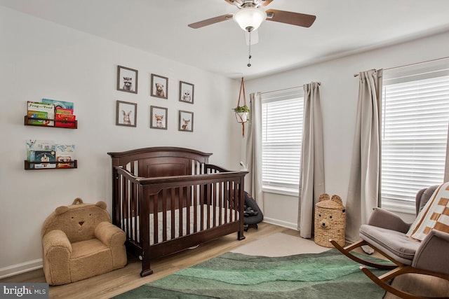 bedroom with a nursery area, wood finished floors, a ceiling fan, and baseboards