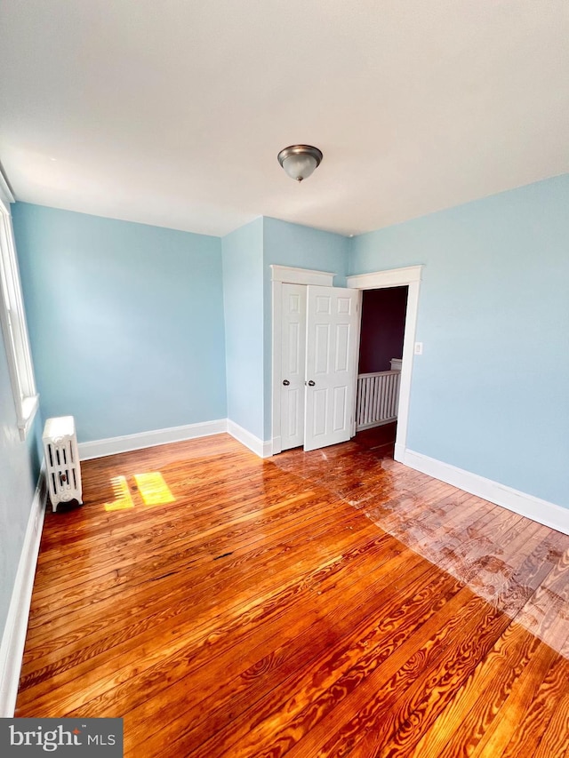 2328 W Lexington St, Baltimore, MD 21223 - unfurnished bedroom with radiator heating unit, baseboards, wood finished floors, and a closet