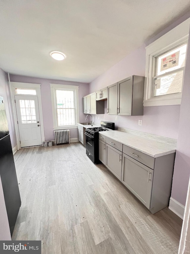 2328 W Lexington St, Baltimore, MD 21223 - kitchen featuring radiator, black range with gas stovetop, gray cabinetry, and light wood-type flooring