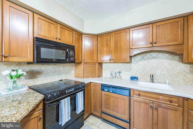 kitchen with black appliances, brown cabinets, a sink, and a textured ceiling