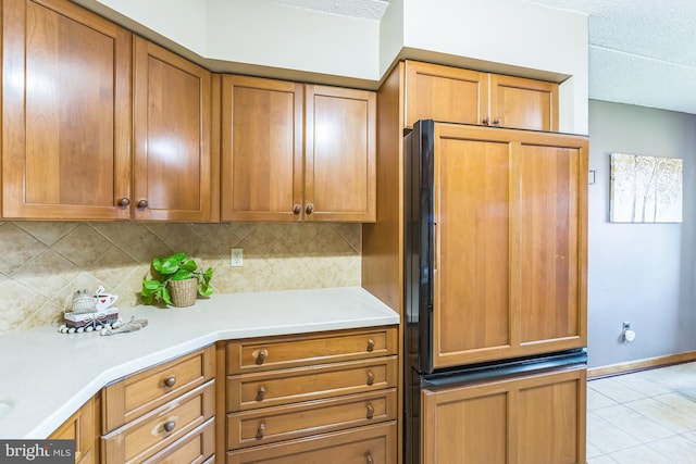 kitchen featuring paneled fridge, light countertops, brown cabinetry, light tile patterned floors, and tasteful backsplash