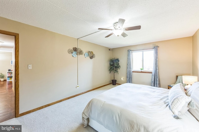 bedroom featuring light colored carpet, baseboards, a ceiling fan, and a textured ceiling