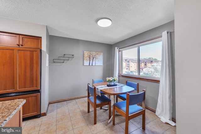 dining space with baseboards, a textured ceiling, and light tile patterned floors