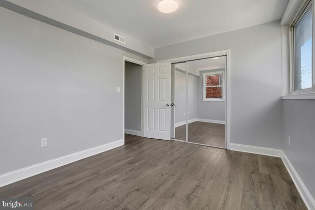 unfurnished bedroom featuring visible vents, baseboards, a closet, and wood finished floors
