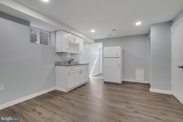 kitchen with freestanding refrigerator, light stone countertops, white cabinets, wood finished floors, and baseboards