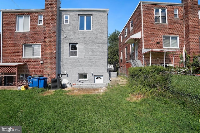 rear view of property with central air condition unit, brick siding, and a lawn