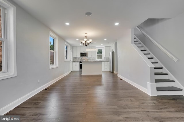 unfurnished living room with visible vents, baseboards, a notable chandelier, dark wood finished floors, and stairway