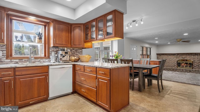 kitchen featuring ceiling fan, brown cabinetry, light stone counters, dishwasher, and a sink