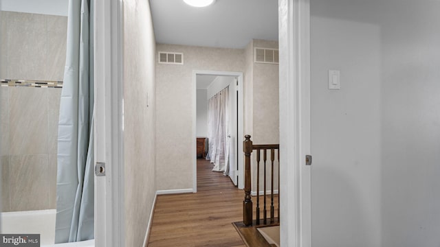 hall with visible vents, baseboards, and wood finished floors