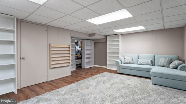 living room featuring a paneled ceiling, wood finished floors, wood walls, and baseboards