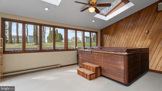 interior space featuring baseboard heating, wooden walls, lofted ceiling with skylight, carpet, and ceiling fan