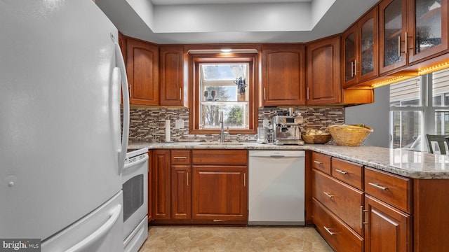 kitchen featuring white appliances, light stone countertops, a sink, brown cabinets, and backsplash
