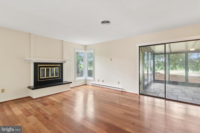 unfurnished living room with baseboard heating, plenty of natural light, wood finished floors, and a glass covered fireplace