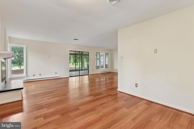 unfurnished living room featuring baseboard heating, light wood finished floors, and healthy amount of natural light