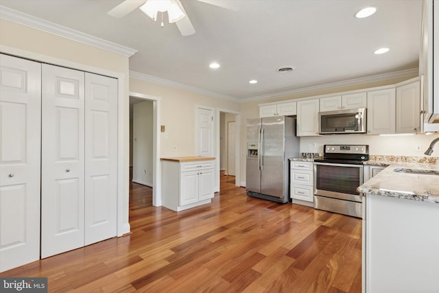 kitchen featuring appliances with stainless steel finishes, a sink, light wood-style flooring, crown molding, and ceiling fan