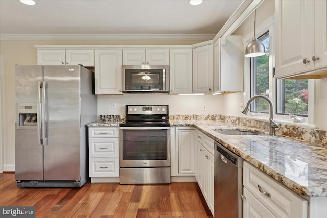 kitchen with appliances with stainless steel finishes, a sink, crown molding, light wood-type flooring, and light stone countertops